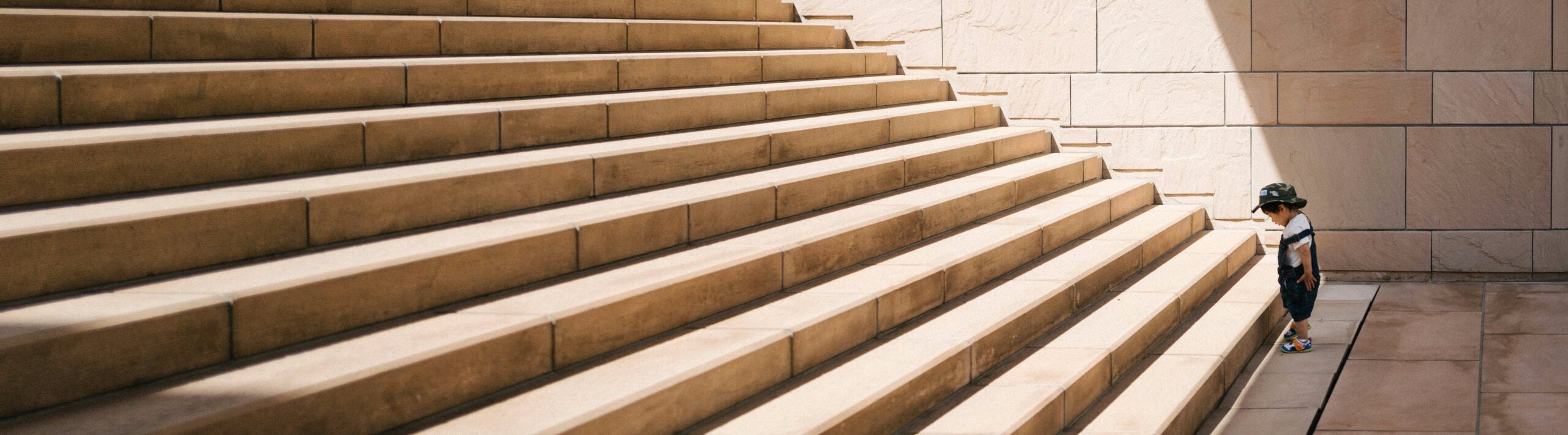 Child at bottom of steps looking like about to take a first step upwards - Photo by Jukan Tateisi on Unsplash